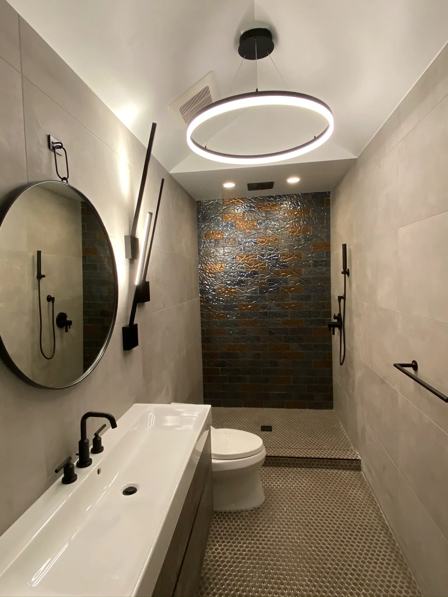 Modern bathroom with circular mirror and textured shower wall — Ariana Designs