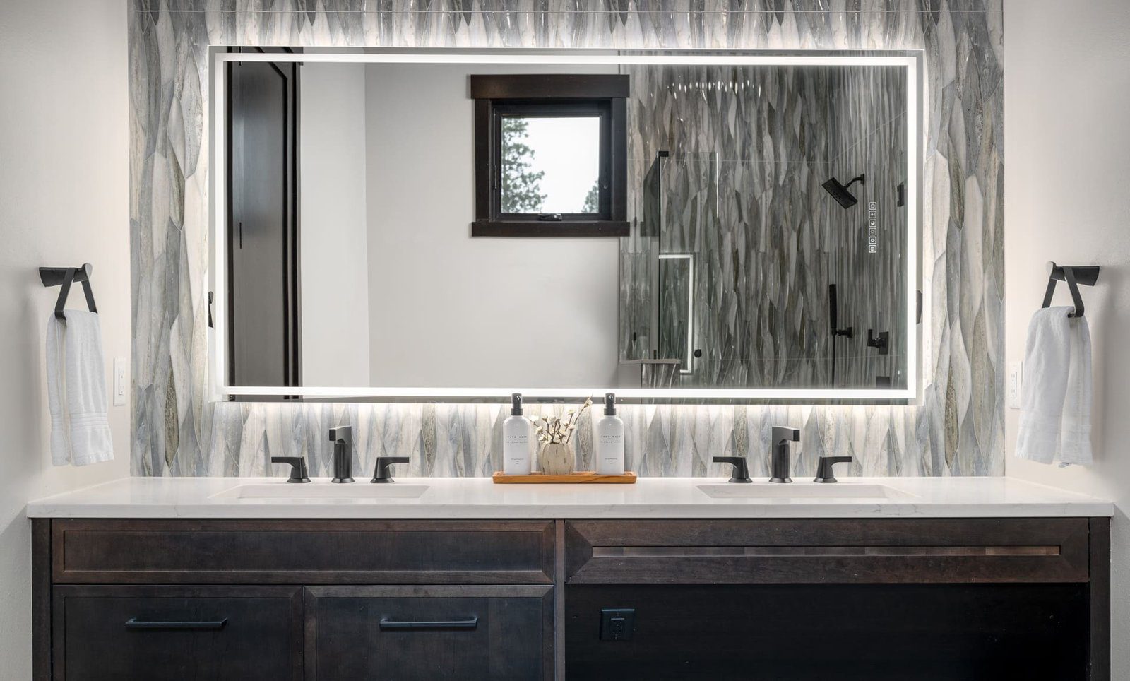 Stylish modern bathroom with double sink vanity, elegant mirror, and textured gray tiles.